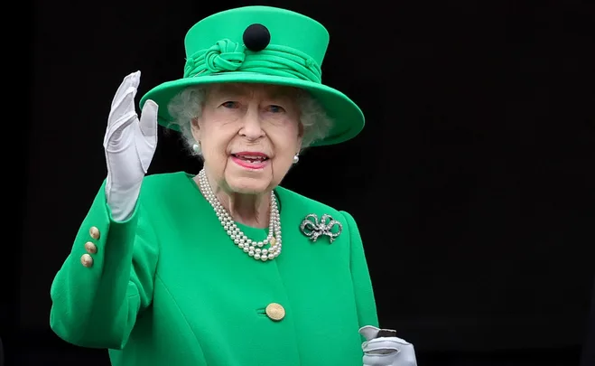 Queen Elizabeth II in a green outfit and hat, waving during the Platinum Jubilee celebration.