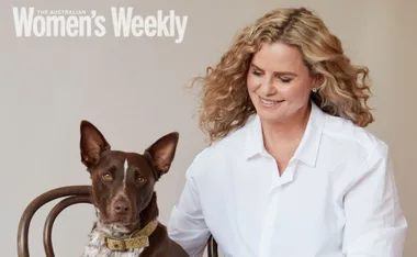 A woman in a white shirt sits smiling beside a brown and white dog on a chair, featured in a magazine cover.