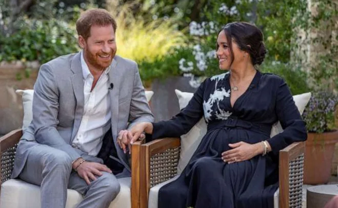 A couple sitting outdoors, holding hands; the man is in a grey suit, the woman in a black dress, smiling at each other.