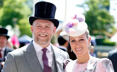 A couple dressed in formal attire with hats, smiling outdoors at a daytime event.
