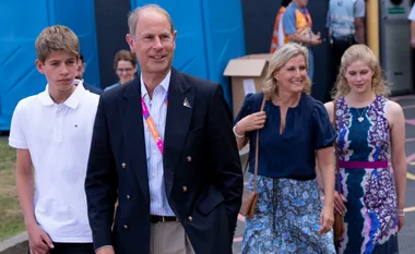 A family of four walks outdoors, with a teenage boy in a white shirt and three adults in smart-casual attire.