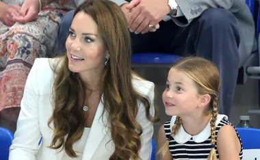 A woman and a girl sit close, smiling and looking ahead, with a crowd in the background.