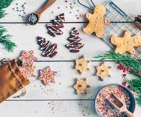 Assorted Christmas cookies, including gingerbread men and tree shapes, on a wooden table with sprinkles and greenery.