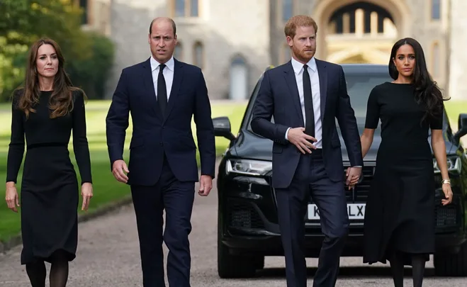 Four individuals in formal black attire walk side by side on a path outside a building, with a car in the background.