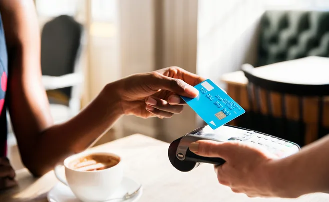 Person paying with a blue credit card using a contactless payment terminal at a cafe.