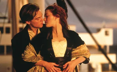 A couple embracing on a ship's deck at sunset, showing affection.