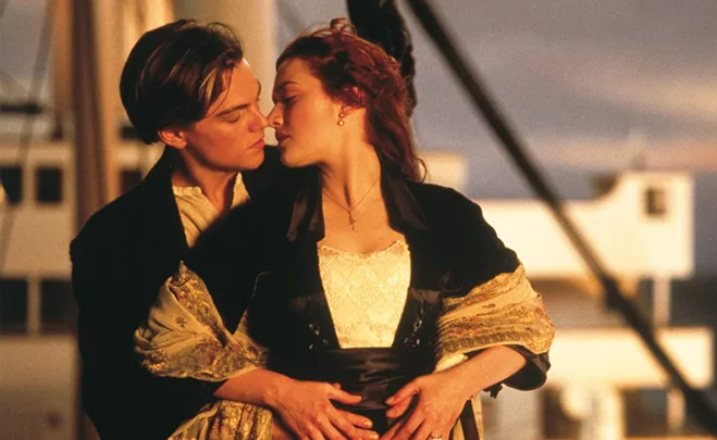 A couple embracing on a ship's deck at sunset, showing affection.