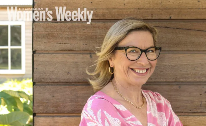 Woman in glasses and pink top smiling against a wooden wall with "Australian Women's Weekly" text overlay.