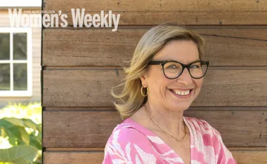 Woman in glasses and pink top smiling against a wooden wall with "Australian Women's Weekly" text overlay.