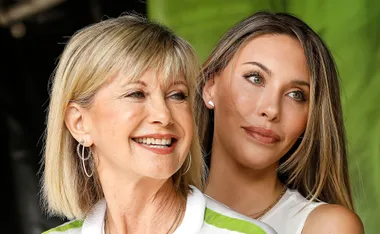 Two women smiling, standing closely with green background.