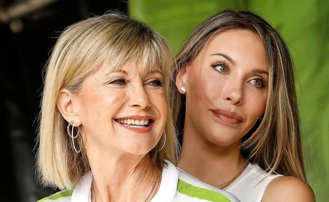 Two women smiling, standing closely with green background.