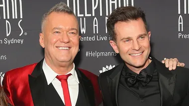 Two smiling men in formal attire at the Helpmann Awards, with a dark background featuring event branding.