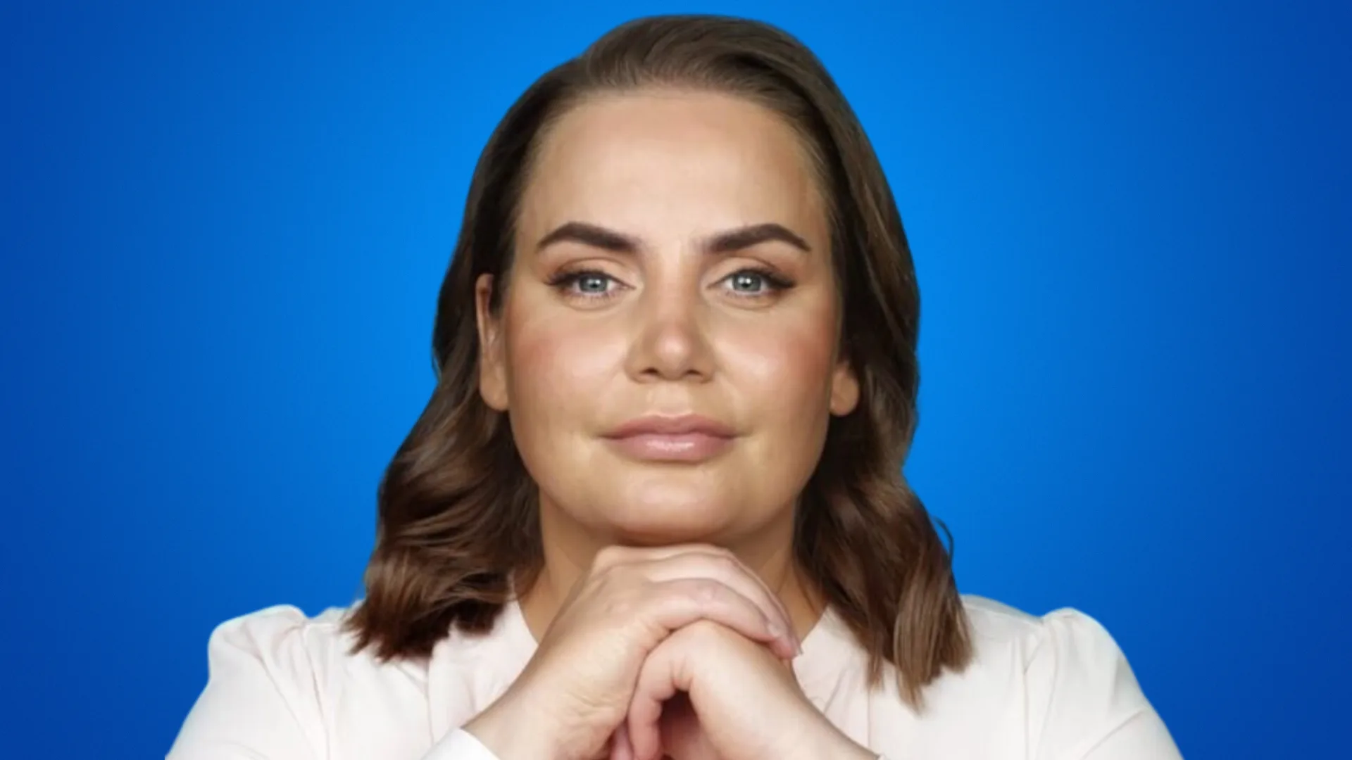 A woman with brown hair and a blue background, resting her chin on her hands.