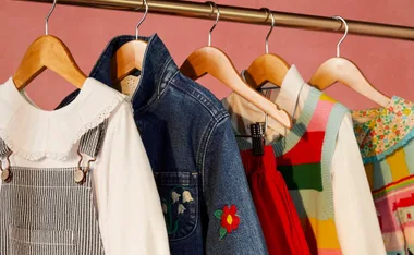 Children's clothing on hangers: a denim jacket, striped overalls, and colorful patterned outfits on a rack.