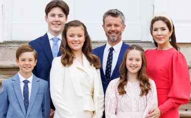Royal family portrait: couple with three children, standing outdoors in formal attire.