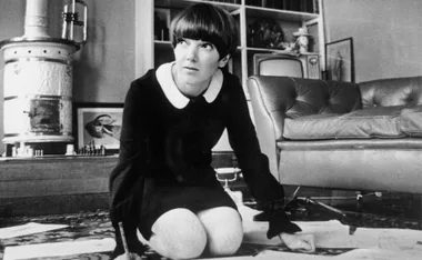 Designer Mary Quant kneeling on a carpet, sketching designs, in a room with vintage decor.