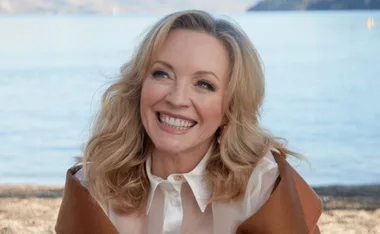 Smiling woman with blonde hair by a serene lake.