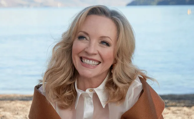 Smiling woman with blonde hair by a serene lake.