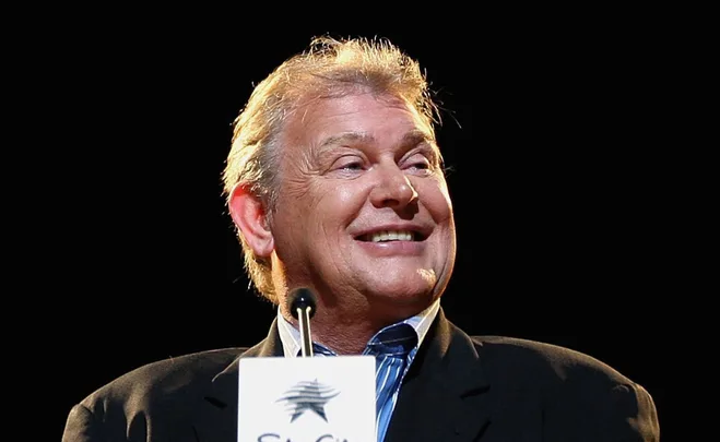 Smiling man in a suit speaking at a podium with a microphone.