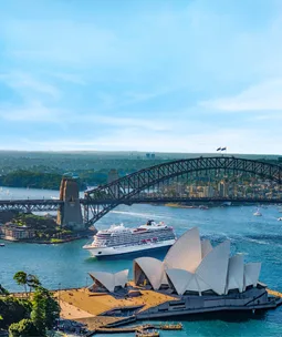 Cruise ship near Sydney Opera House and Harbour Bridge on a sunny day.