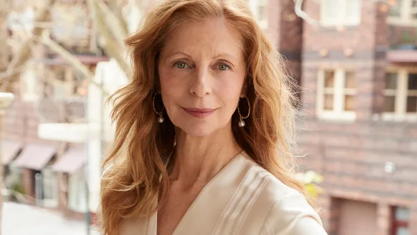 A woman with long red hair wearing a beige dress standing on a decorative balcony, featured in Australian Women's Weekly.