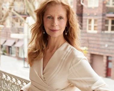 A woman with long red hair wearing a beige dress standing on a decorative balcony, featured in Australian Women's Weekly.