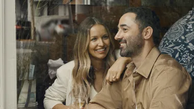 Smiling couple enjoying a drink together indoors by a window.