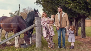 Family of four with a horse in a rural setting, parents holding a baby, and a child with a stuffed toy.