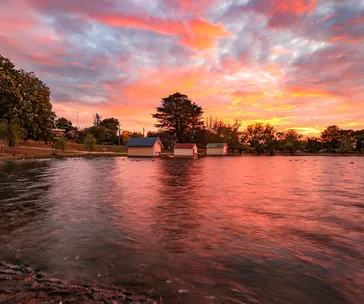 Sunset over Lake Wendouree in Ballarat, Australia, with boathouses and trees reflecting in the calm water.