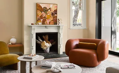 Cozy living room with earth-toned decor, abstract art above fireplace, brown armchair, and round tables.