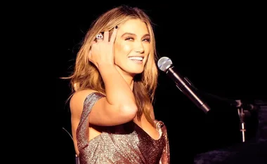 Singer smiling at microphone in sparkling dress on stage.