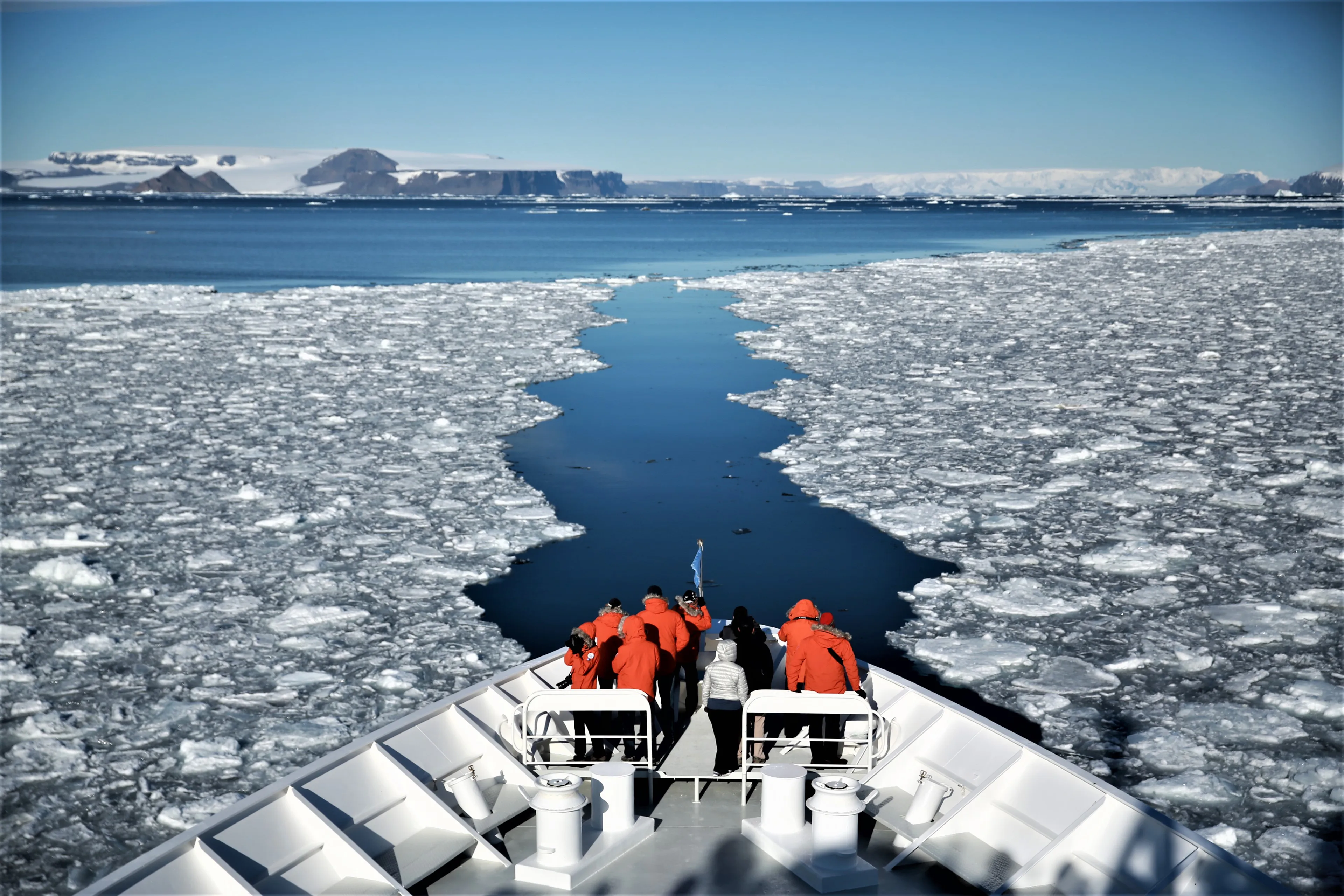 A group of people on board a cruise ship in Antartica with glaciers in the distance