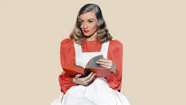 Woman in a red blouse and white apron reading a book, styled with vintage waves and red lipstick.