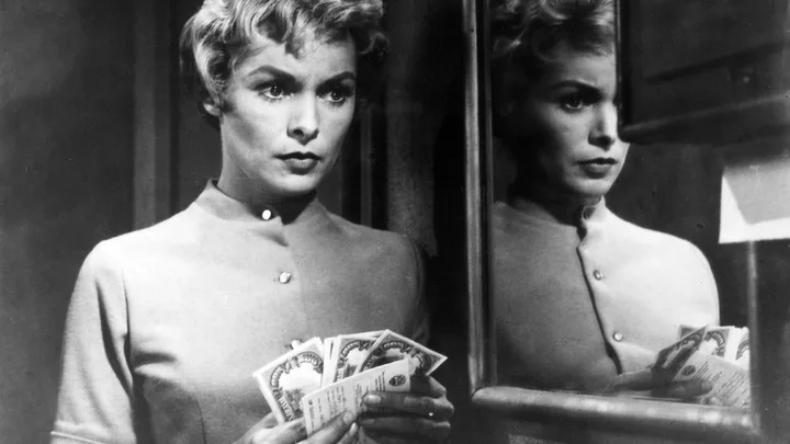 A woman with short hair holds cash, looking intensely in a mirror reflection. Black and white image.