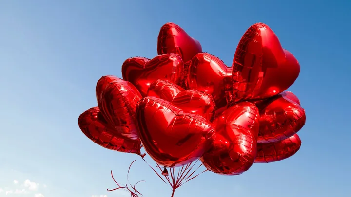 A cluster of red heart-shaped balloons floating against a clear blue sky.