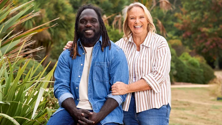 A man in a blue shirt and a woman in a striped shirt smiling outdoors with greenery in the background.
