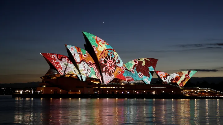 Sydney Opera House at dusk, featuring vibrant Indigenous-inspired light projections on its iconic sails.