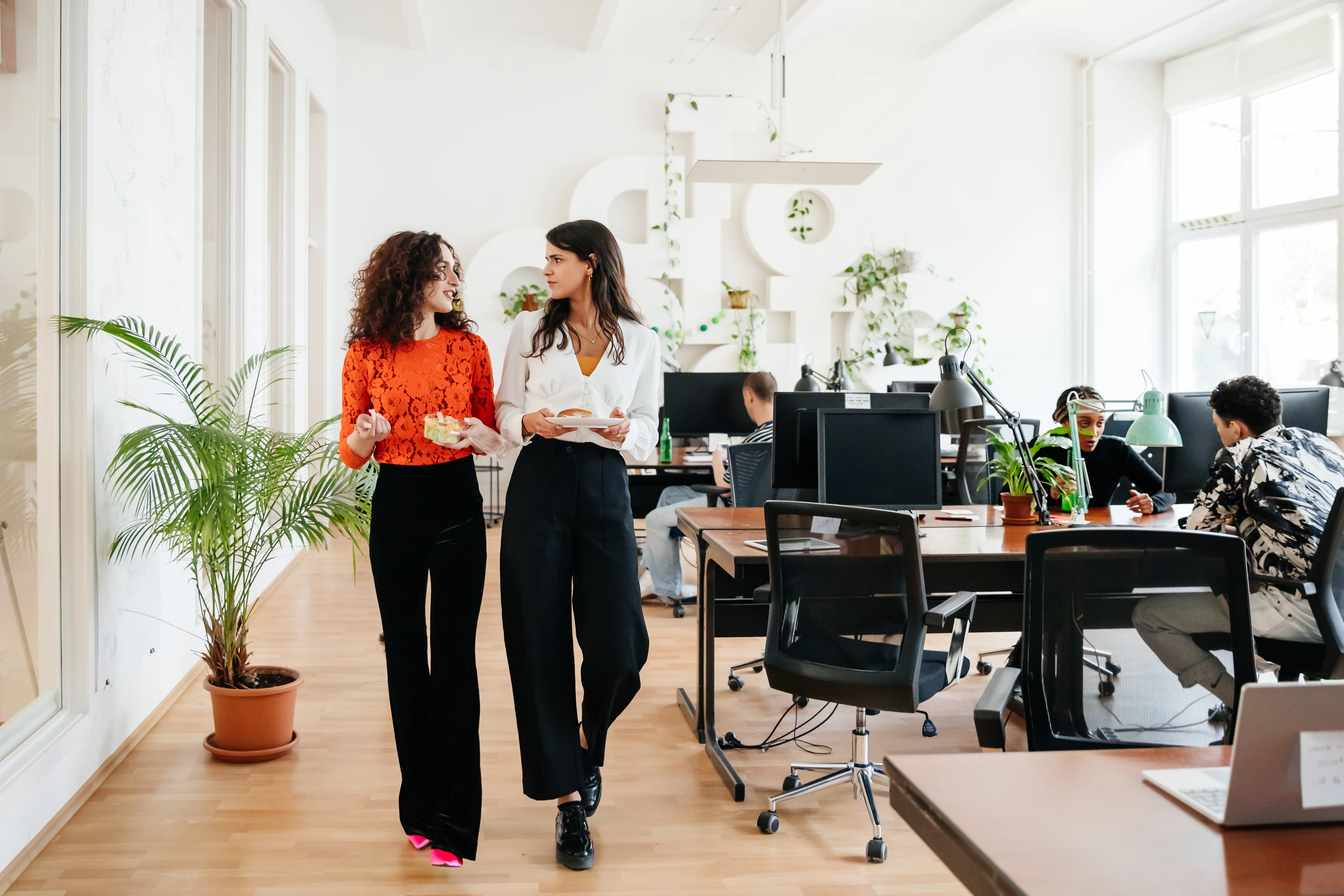 Two office colleagues walking past some computer desks.