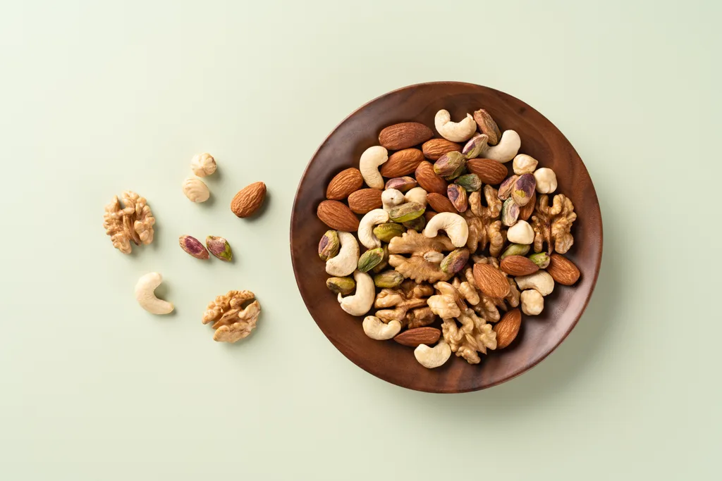Assorted Nuts of Almond,Cashew,Hazelnut,Pistachio and Walnut Mixed in a Wood Bowl on Green Background Directly Above View. Nuts help with liver health.