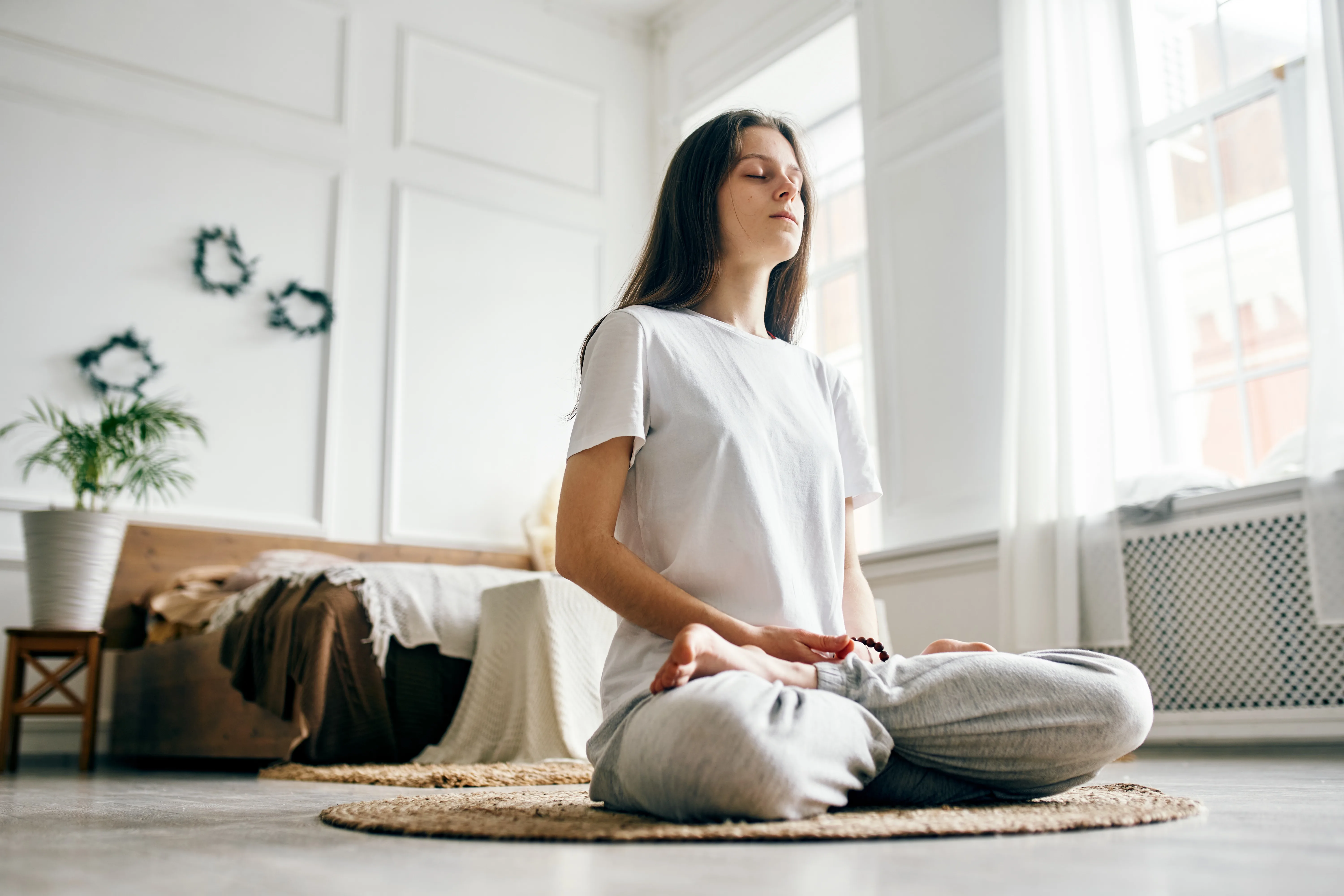 Full length of woman practicing breathing exercise. Young woman with eyes closed sitting in lotus position. She is living room at home.