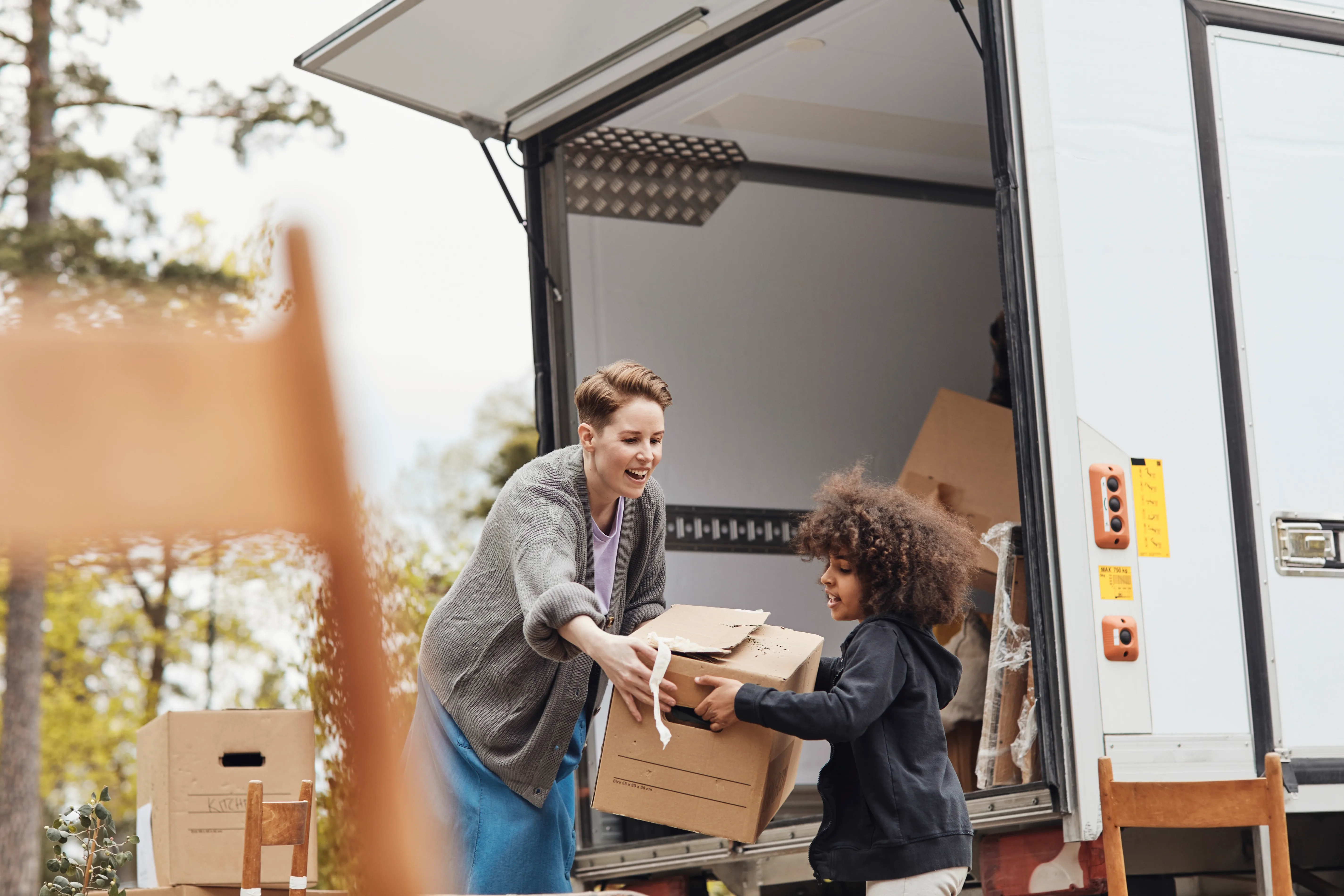 A child helps woman load boxes into a truck to move house.