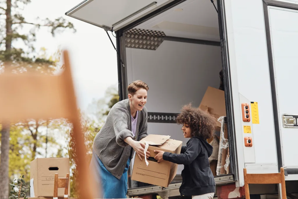 A child helps woman load boxes into a truck to move house.