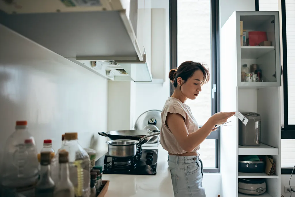 A woman holding paper various expense bills and plans for personal finances at her home.