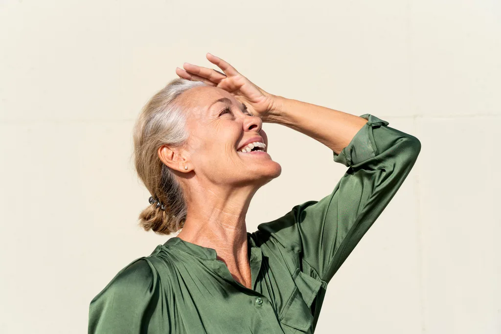 Happy mature woman shielding eyes on sunny day.