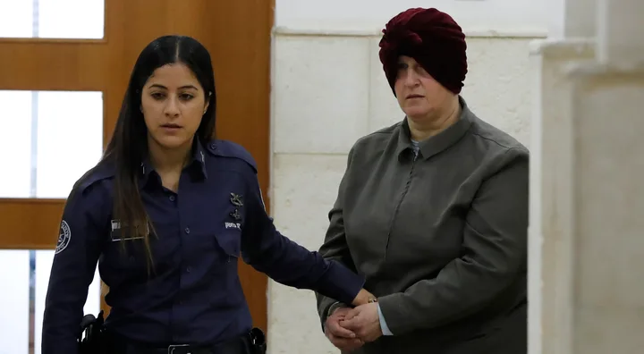 A woman in a police uniform escorts another woman with a head covering through a hallway.