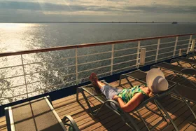 A middle aged woman in a sunbonnet relaxes on the top deck of a cruise ship during her vacation at sea