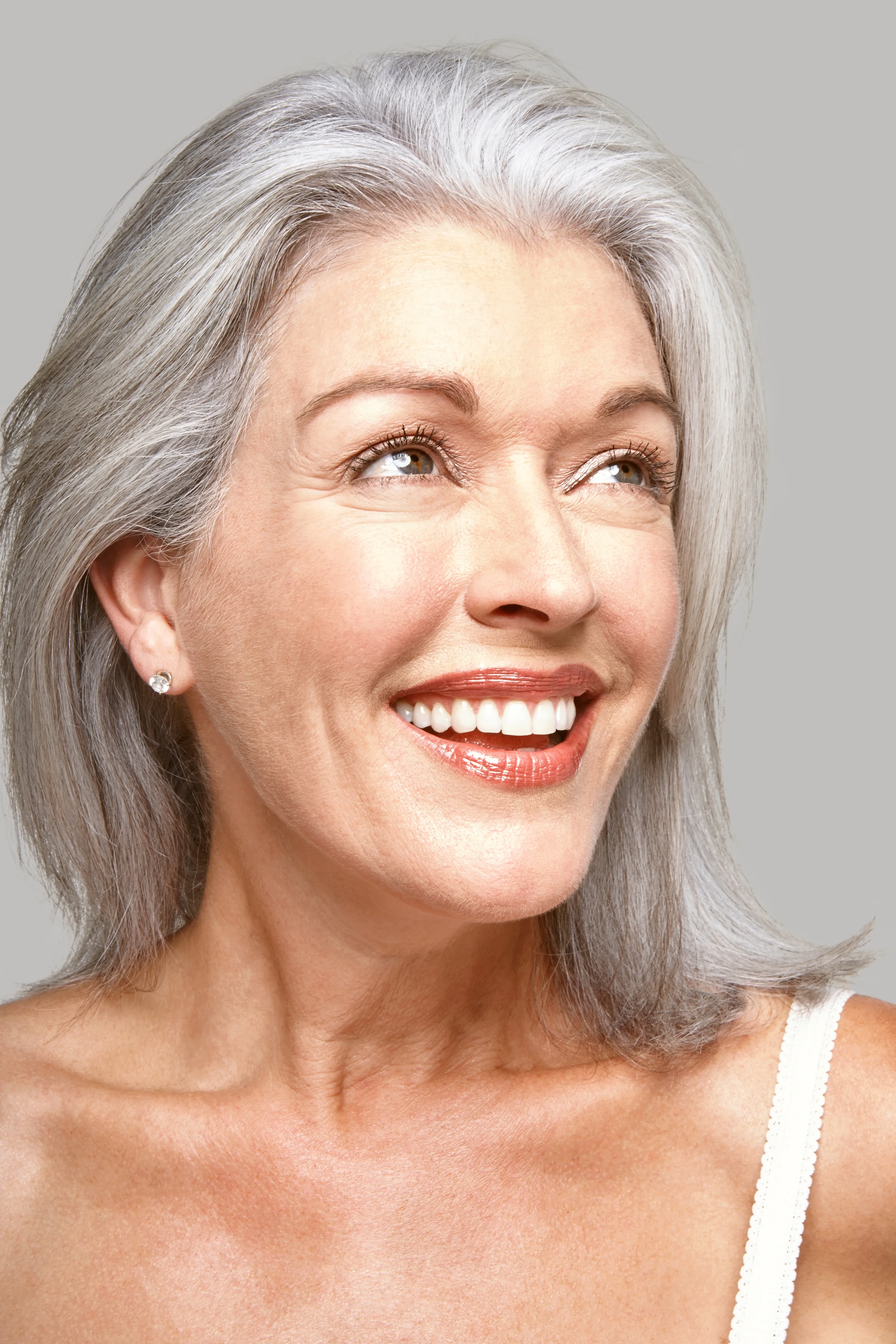 Close-up portrait of mature woman smiling with grey hair looking up.