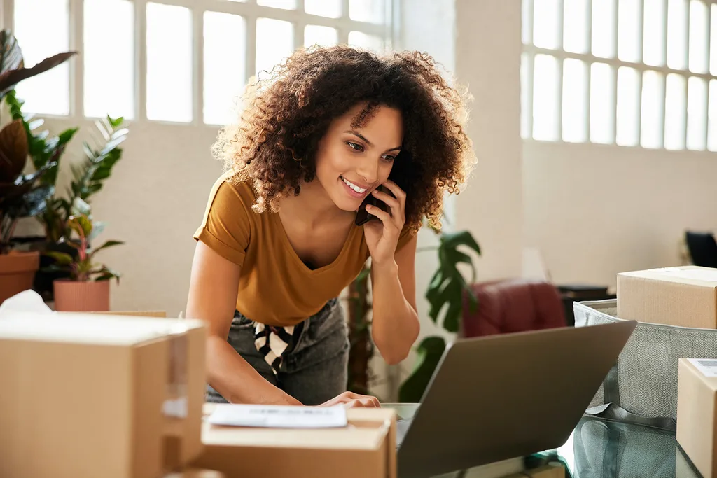 Woman on the phone and also working on her laptop. 