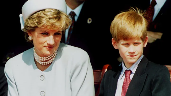 A woman in a white hat and pearls sits beside a boy in a suit and tie at an outdoor event.