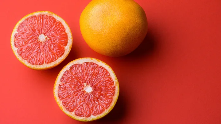 Whole and halved grapefruit on a red background.